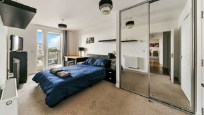 Ein Schlafzimmer mit einem großen Bett, einem Schreibtisch, einem Spiegel und einer Schiebetür zu einem weiteren Raum.