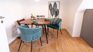 Ein Essbereich mit einem Holztisch, zwei blaugrünen Stühlen und einem gewebten Teppich.