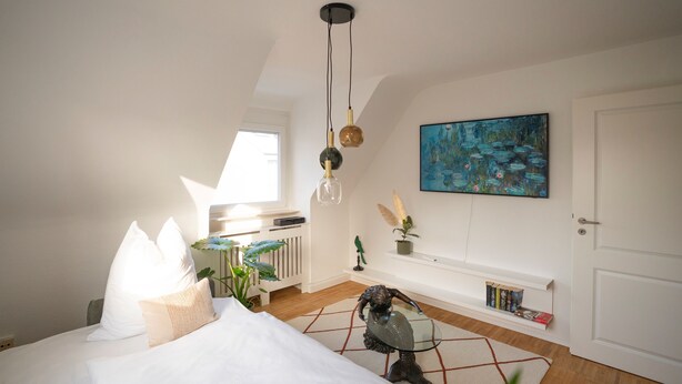 Ein Schlafzimmer mit einem Bett, einem Glastisch, einer dekorativen Fischskulptur, einem Gemälde und einem Bücherregal.