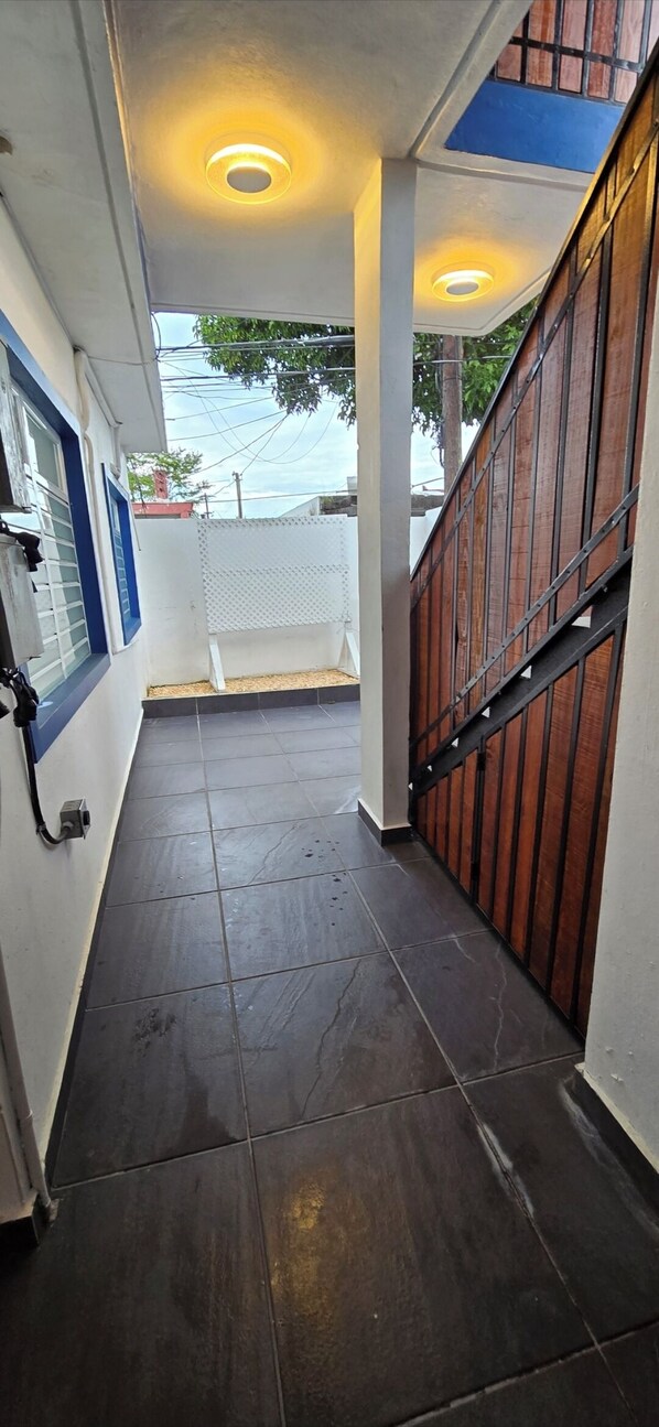 Un pasillo con piso de baldosas, una escalera con barandas de madera y una pared blanca con ventana y puerta.