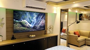 A modern living room with a large flat-screen TV mounted on a wooden console, a beige sofa, and a small round table.