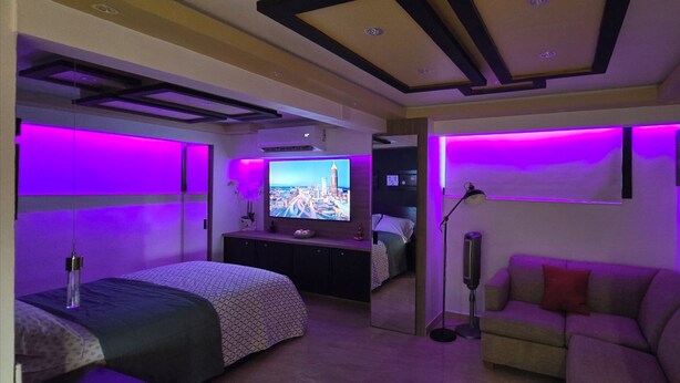A modern bedroom with a bed, a sofa, a TV, and ambient purple lighting.