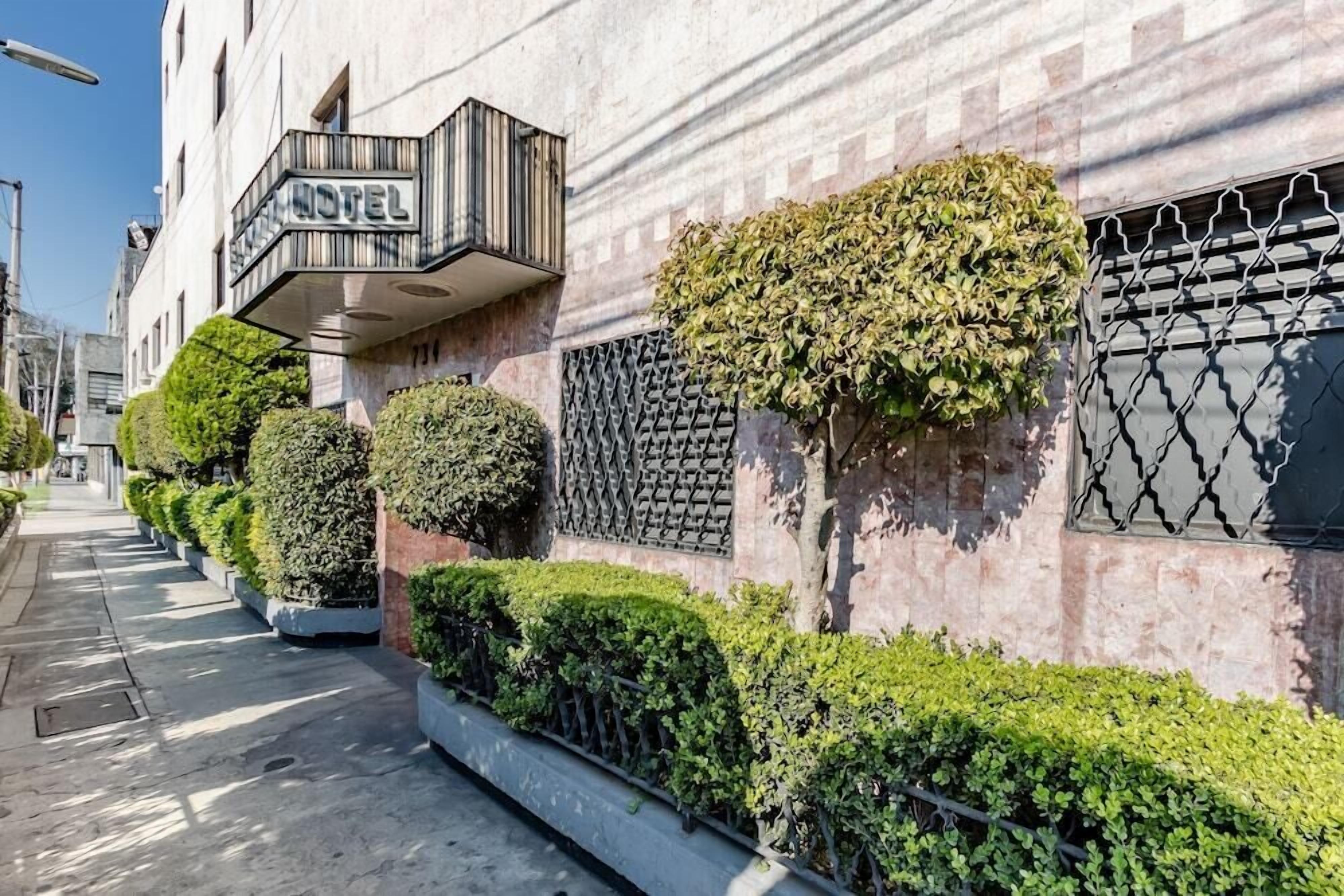 Un hotel con balcón, setos bien cuidados y una reja de metal.