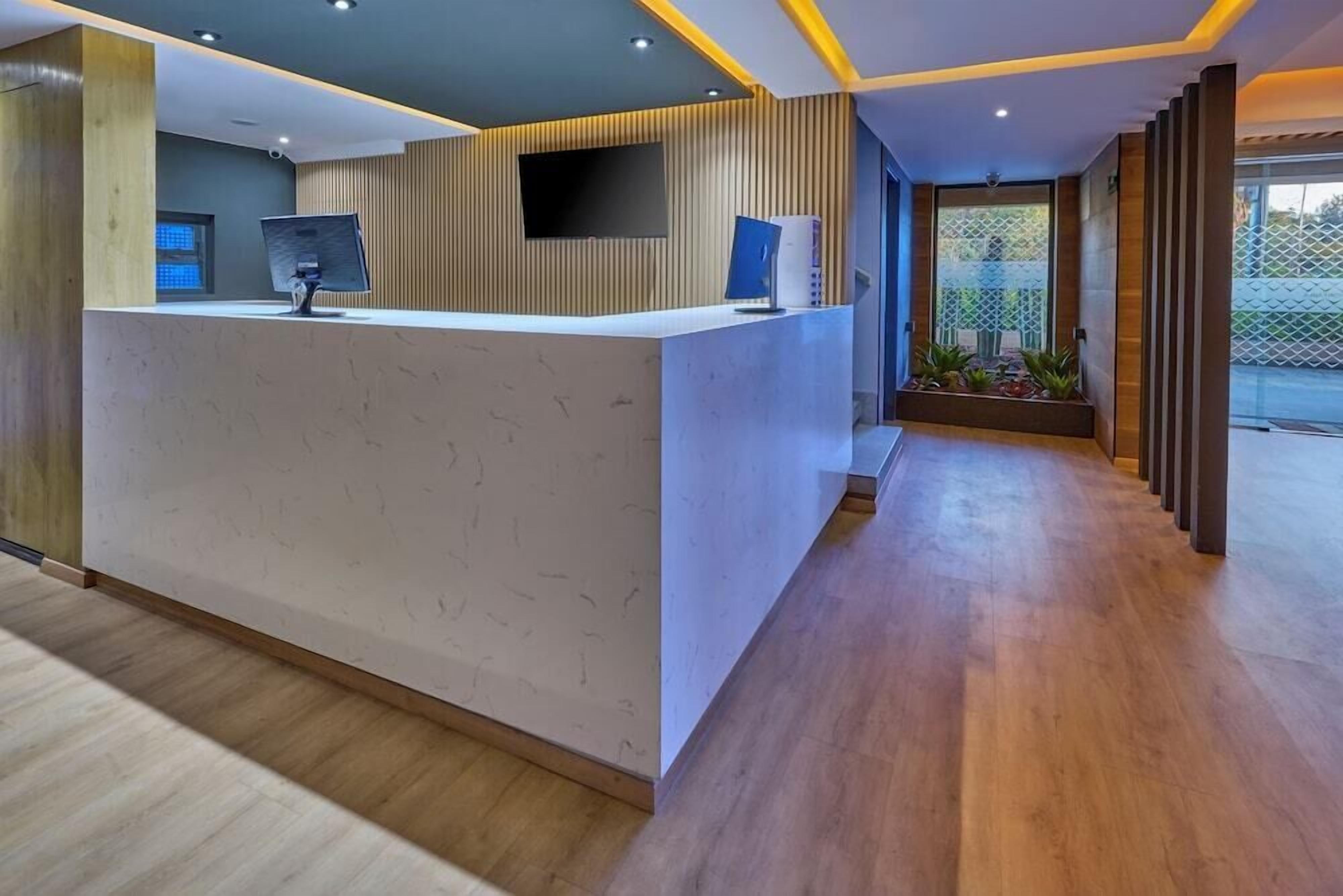 Un área de recepción con diseño moderno, que incluye un mostrador de recepción, un televisor de pantalla plana y un espacio de estar con plantas.