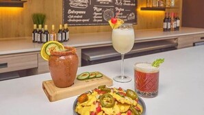 A bar area with a chalkboard menu, a variety of bottles on shelves, and a plate of nachos with a drink in front. - Hotel el Patio Cdmx (Mexico City)
