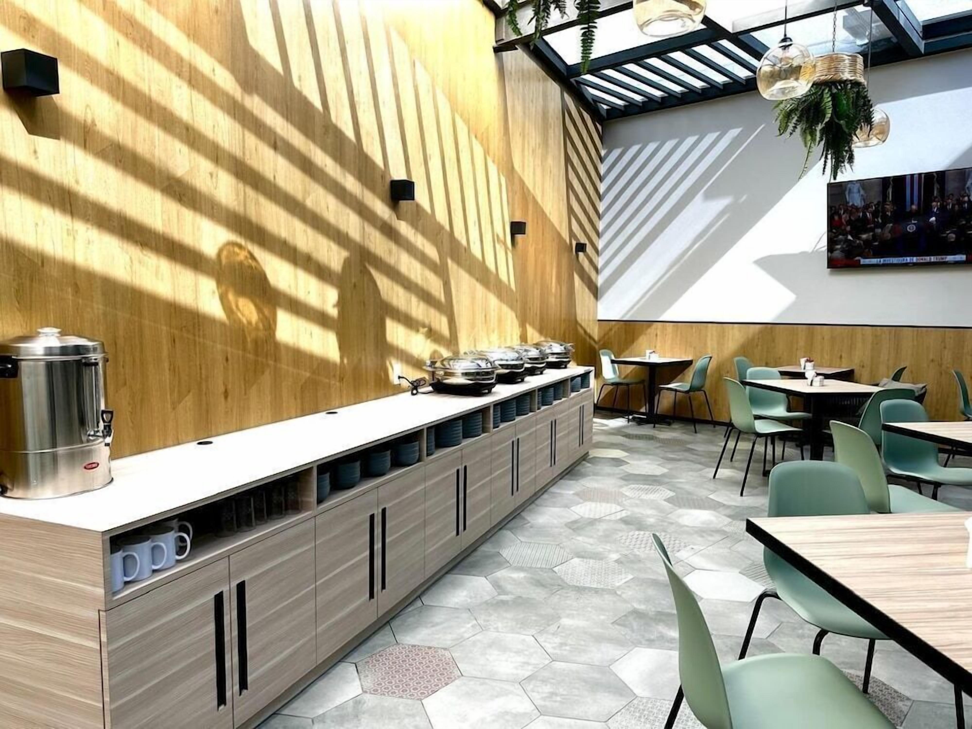 Un café moderno con una barra alargada, suelo de patrón hexagonal y sillas verdes.