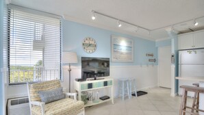 A living room with a sofa, TV, and a dining area with stools.