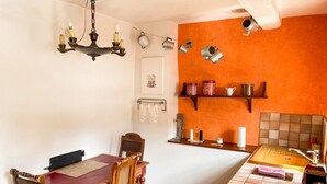 Eine Küche mit Holztisch und Stühlen, einer Hängeleuchte und einem Regal mit Küchenutensilien.