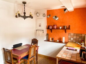 Una cocina con una mesa y sillas de madera, una lámpara colgante y una estantería con utensilios de cocina.