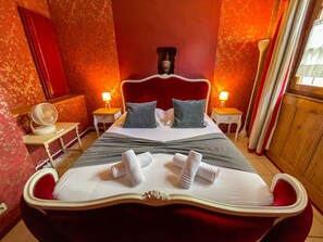 Un lit avec une tête de lit rouge, deux tables de chevet et un ventilateur.
