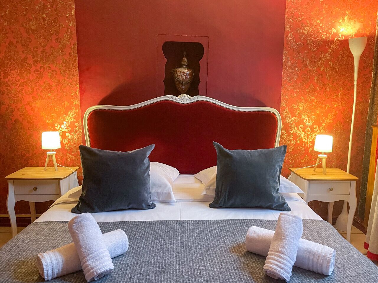 A neatly made bed with two pillows, two bedside tables with lamps, and a red headboard.