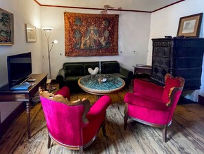 Un salon avec un canapé vert, deux fauteuils rouges, une table basse, un téléviseur et une tapisserie au mur.