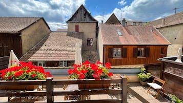 Une cour avec des bancs en bois, des fleurs rouges et des bâtiments traditionnels aux toits de tuiles.