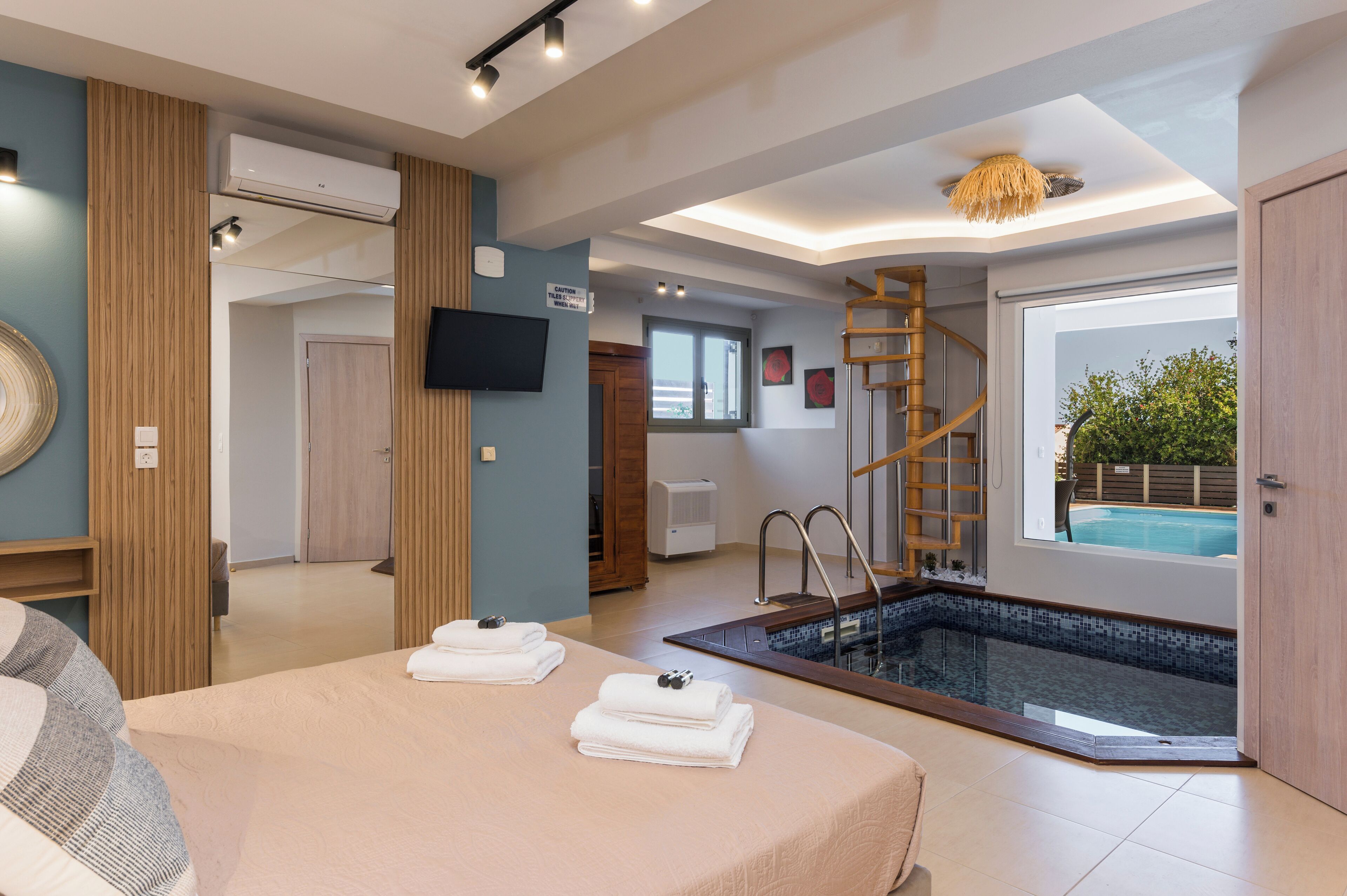 A modern hotel room with a pool, a wooden staircase, and a flat-screen TV.