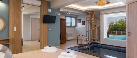 A modern hotel room with a pool, a wooden staircase, and a flat-screen TV.