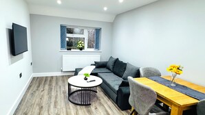 A modern living room with a grey sofa, a round coffee table, and a dining table with chairs. - Stylish Stay in Birmingham (Oldbury)
