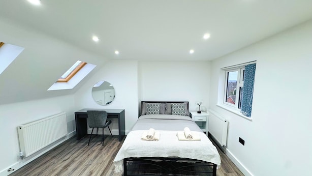 A bedroom with a skylight, a bed with a striped bedspread, a desk with a chair, and a window with curtains. - Stylish Stay in Birmingham (Oldbury)