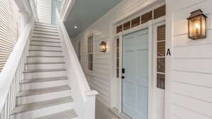 A staircase leading to a light blue door with a small window, flanked by white walls and a lantern. - The Saint's Suite - brand new 3 Bed/3 EnSuite Bath, 1 Block to King (Charleston)
