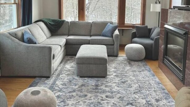 Una sala de estar acogedora con un sofá seccional, un reposapiés y una alfombra estampada.