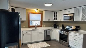 Una cocina compacta con gabinetes blancos, un refrigerador de acero inoxidable, un microondas, un horno y un lavavajillas.