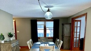 Comedor con mesa y sillas de madera, una lámpara de araña y vistas de la ciudad a través de amplios ventanales.