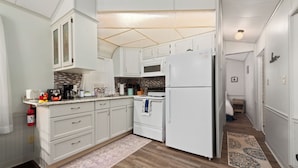 A kitchen with white cabinets, a microwave, a stove, and a refrigerator. There is a patterned rug on the floor.