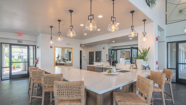 A modern kitchen with a large island, pendant lighting, and wicker chairs.