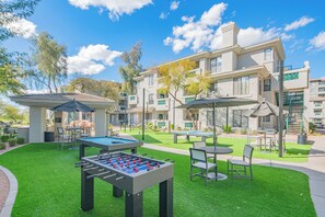 An outdoor pool area with a foosball table, outdoor seating, and a building in the background. - Executive Golf Group Side by Side Suites|Clubhouse (Scottsdale)