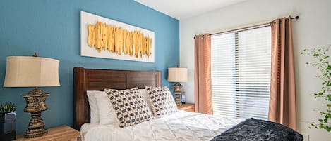 A bedroom with a bed, two nightstands, a ceiling fan, a window with blinds, and a wall art piece.