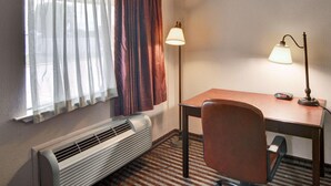 A hotel room with a bed, a desk with a chair, a lamp, and a heater. - Rodeway Inn Gainesville I-35 (Gainesville)