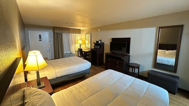 A hotel room with two beds, a desk with a TV, a mirror, and a lamp. - Rodeway Inn Gainesville I-35 (Gainesville)