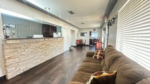 A spacious living area with a stone accent wall, a brown sofa, and a kitchen in the background. - Rodeway Inn Gainesville I-35 (Gainesville)