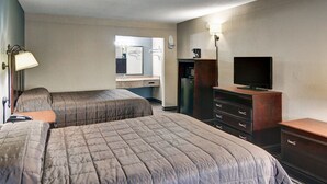A hotel room with two beds, a dresser, a television, a mirror, and a coffee maker. - Rodeway Inn Gainesville I-35 (Gainesville)