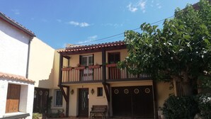 A two-story building with a balcony, a wooden bench, and a paved courtyard. - Unique, comfortable apartment with beautiful view, quiet location. (Ansignan)