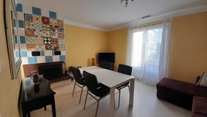 A living room with a tiled wall, a fireplace, a dining table with chairs, a sofa, and a television. - Unique, comfortable apartment with beautiful view, quiet location. (Ansignan)