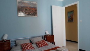 A bedroom with a bed, pillows, a nightstand, a lamp, and a door. - Unique, comfortable apartment with beautiful view, quiet location. (Ansignan)