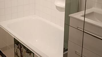 A bathroom with a white bathtub, a glass shower enclosure, and a tiled floor.