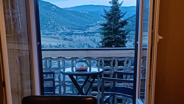A balcony with a table and chairs, a view of a mountainous landscape, and a door leading to an outdoor area. - Unique, comfortable apartment with beautiful view, quiet location. (Ansignan)