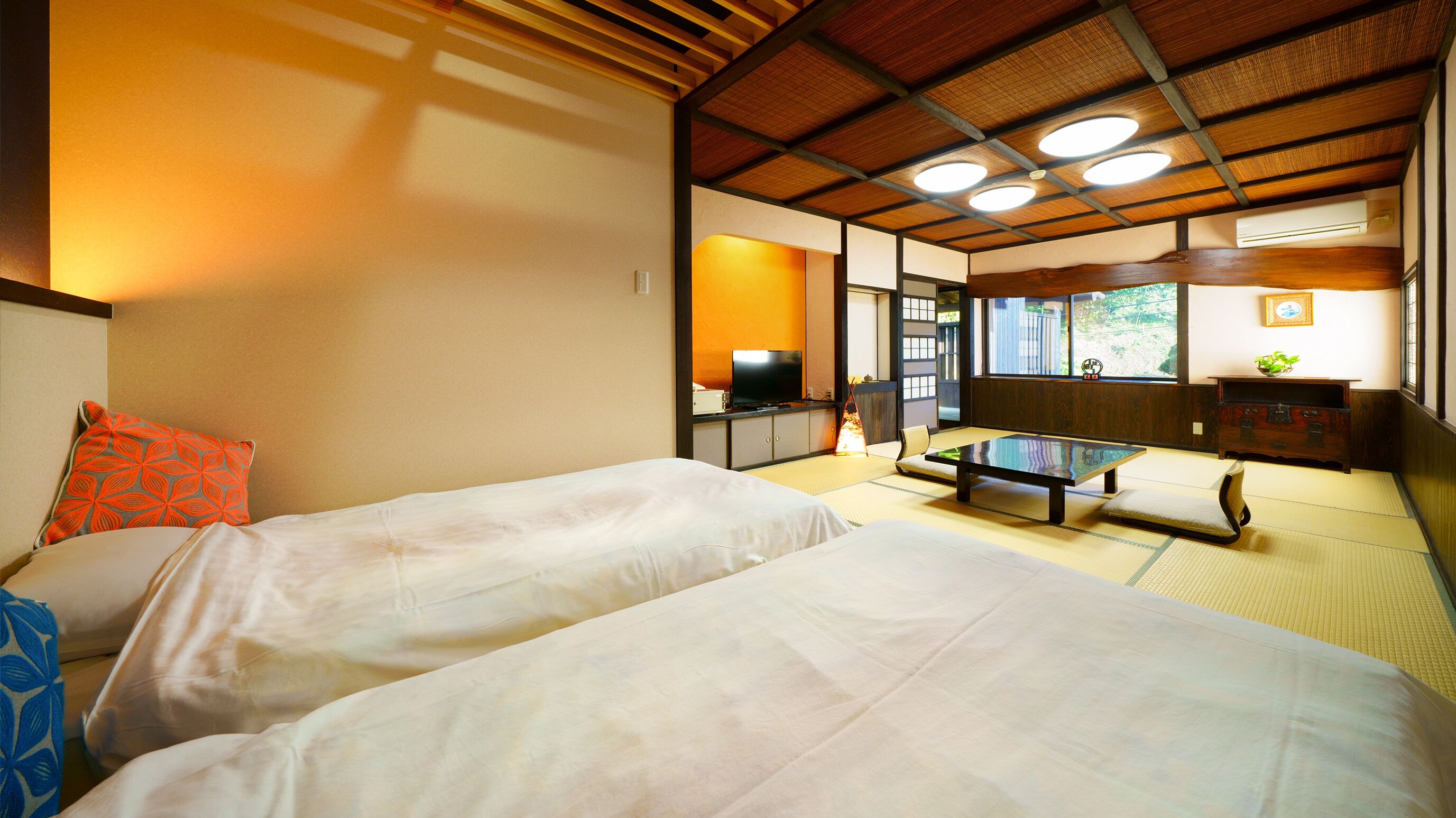 Habitació tradicional japonesa amb sòls de tatami, dos llits, una televisió i vista a l'exterior.