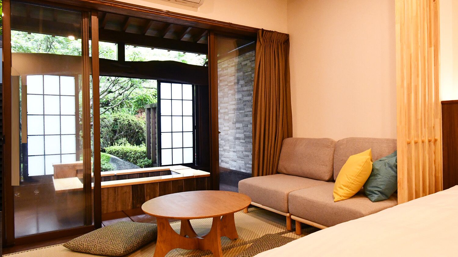 A room with a sofa, a round table, and a sliding door leading to a garden.