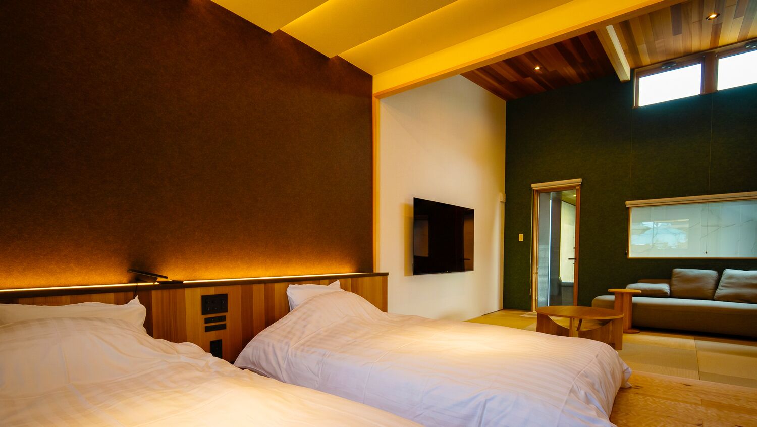 Habitació d'hotel amb dos llits, un sofà, una televisió i una porta corredissa que dona a un balcó.