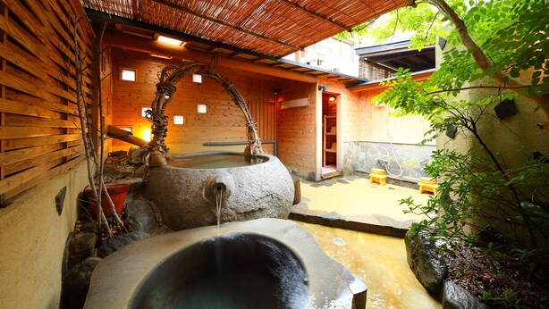A traditional wooden bathhouse with stone hot tubs and a bamboo water feature. - Ureshino Onsen Kujaku (Ureshino)