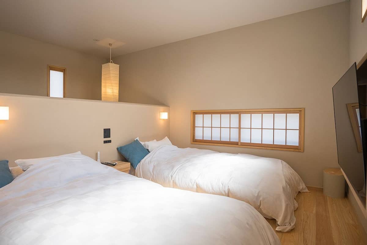 A hotel room with two beds, a window, a hanging light fixture, and a television.