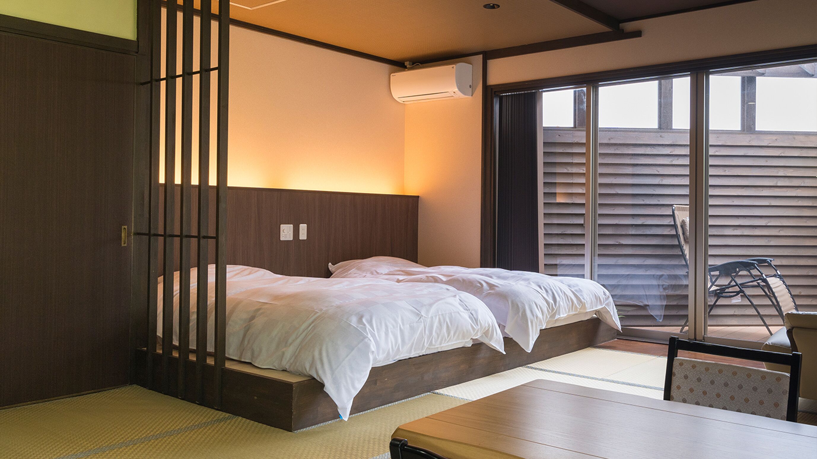 Habitació d'hotel amb un llit, una taula, una cadira, una porta corredissa i una finestra.