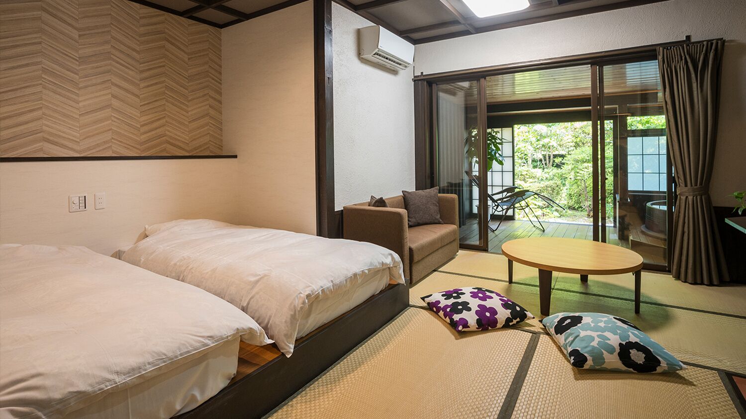 Habitació d'hotel amb dos llits, un sofà, una taula petita, esteves de tatami i una porta corredissa de vidre a l'exterior.