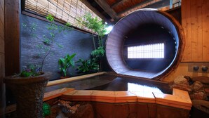 A circular wooden structure with a window, surrounded by plants and a stone wall. - Ureshino Onsen Kujaku (Ureshino)