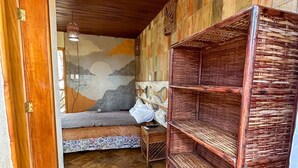 Een kamer met een bed, een klein tafeltje, een plank en een muurschildering.