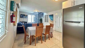 Una cocina moderna con un refrigerador de acero inoxidable, un comedor con mesa y sillas, y una escalera que lleva a una sala de estar.