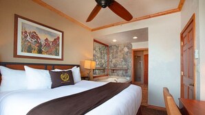 Hotelkamer met een groot bed, een plafondventilator, een stenen open haard en een schilderij van bergen aan de muur.