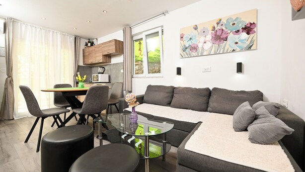 A modern living room with a sofa, ottomans, a glass coffee table, and a dining area with chairs and a table. - New, close to the beach apartment with parking (Mastrinka)